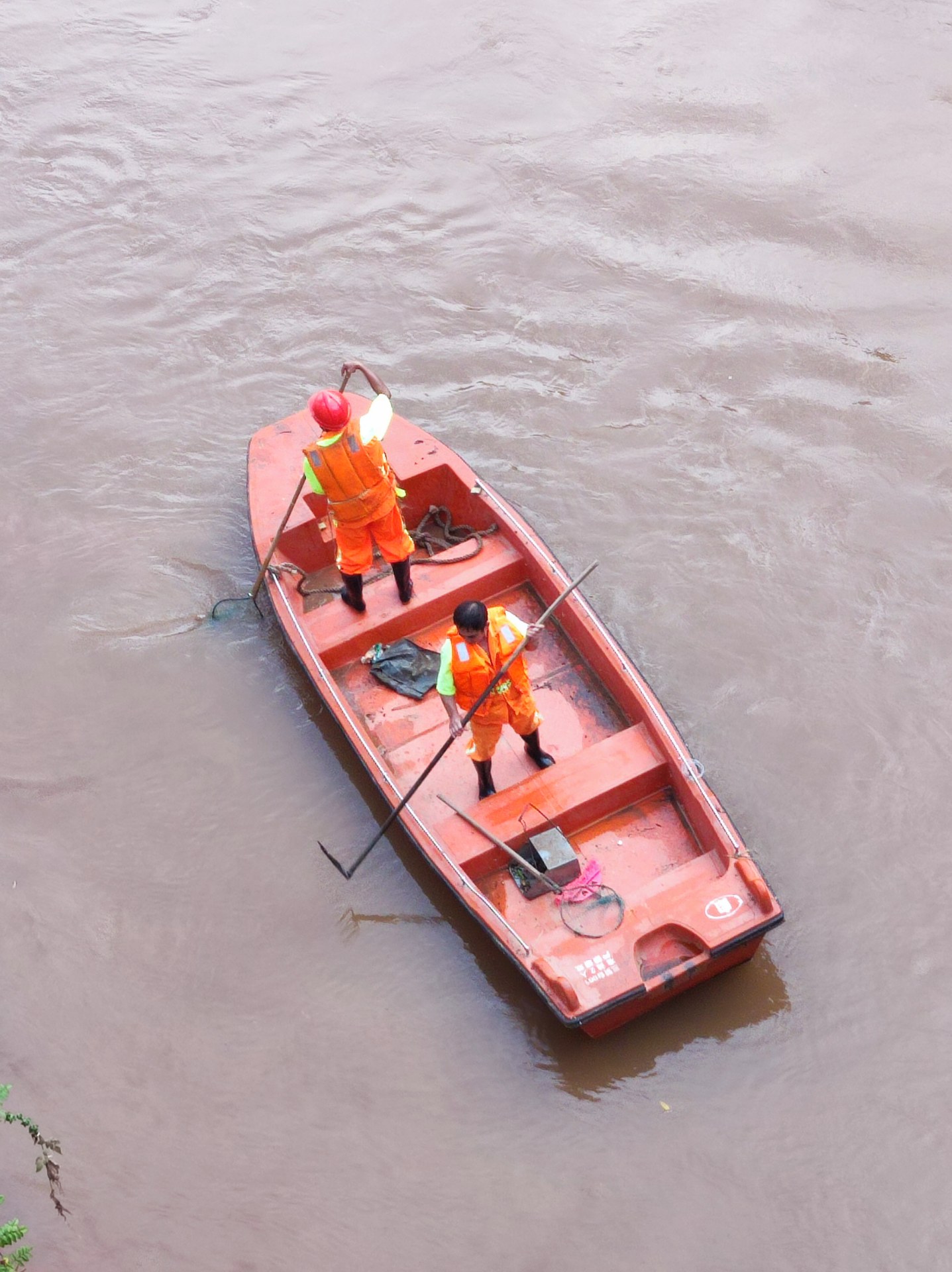 河道垃圾的小船已经搁浅了,两位环卫工人正在用力把打捞船推入河水中