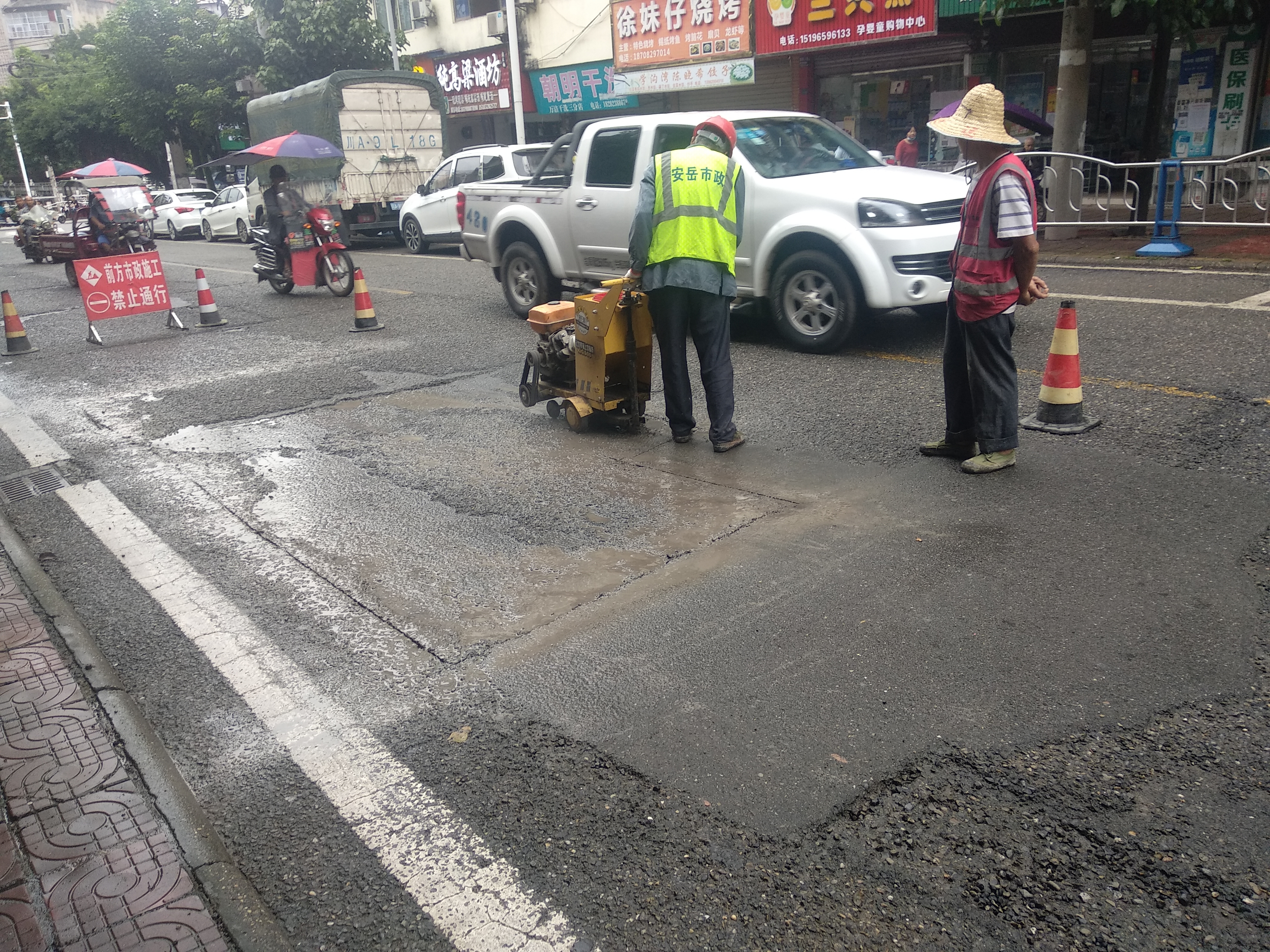 安岳学沟湾路口,工人用机械正在切割凹的沥青路面